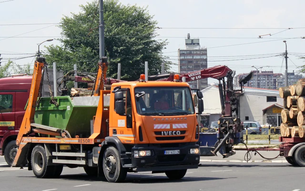 Camion de collecte chargeant une benne à déchets en bord de voie.
