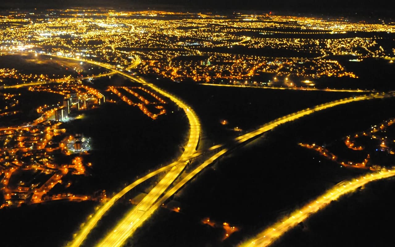 Échangeur autoroutier vu du ciel de nuit, les voies dessinées par les traînées lumineuses des véhicules.