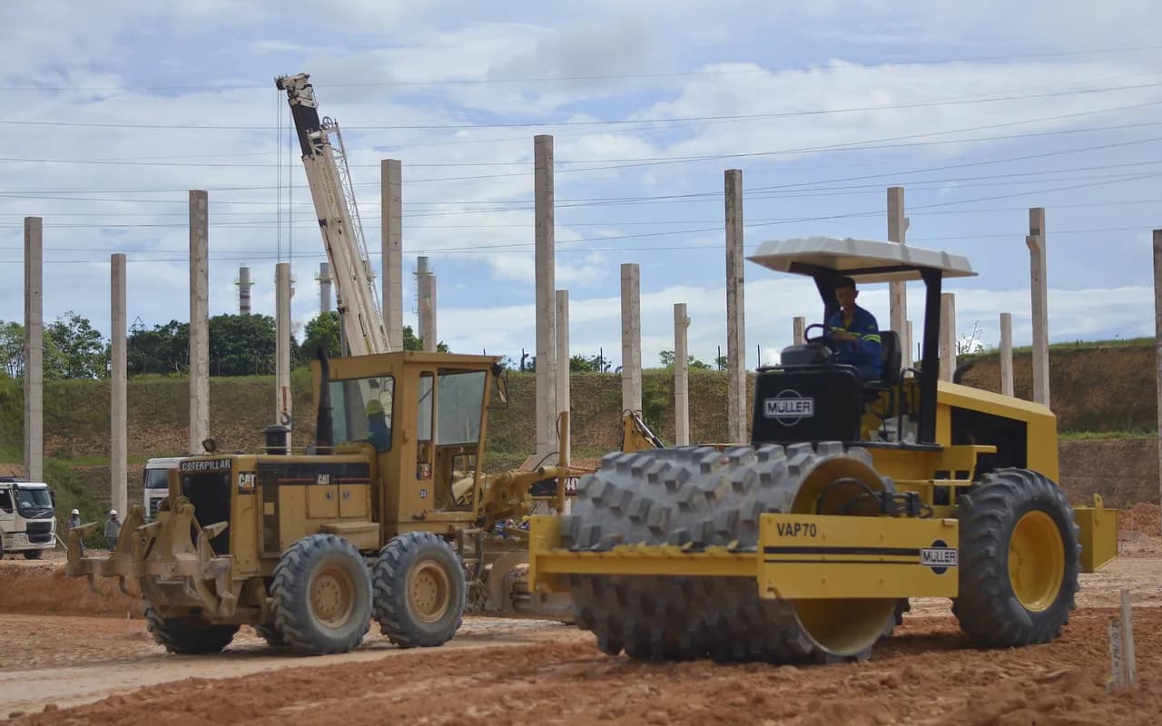 Une niveleuse de chantier à l'arrêt sur une plateforme de terre, en plein soleil.