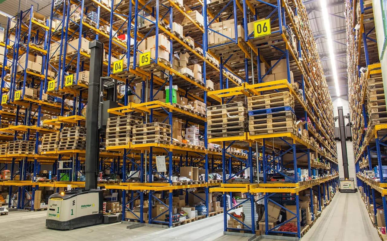 Allée d'un entrepôt à rayonnage grande hauteur, palettes stockées sur plusieurs niveaux sous toiture.
