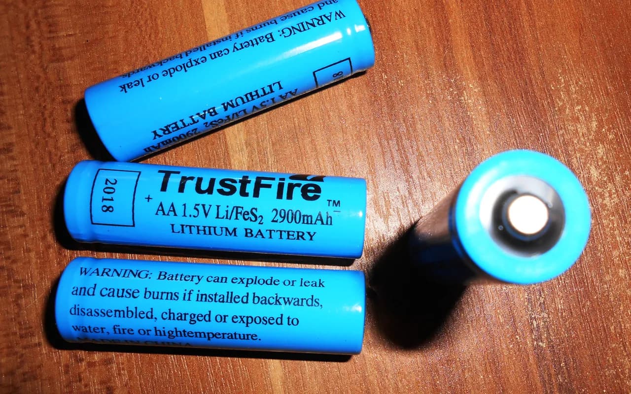 Trois piles AA au lithium-fer marquées Li/FeS2 1,5 V, non rechargeables, posées sur un plan de bois.