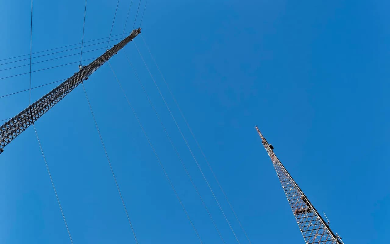 Deux pylônes d'antennes haubanés, vus depuis leur pied contre un ciel dégagé.
