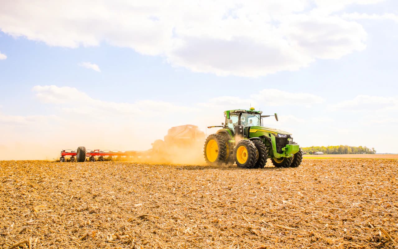 Tracteur agricole tirant une remorque au travail dans un champ labouré.