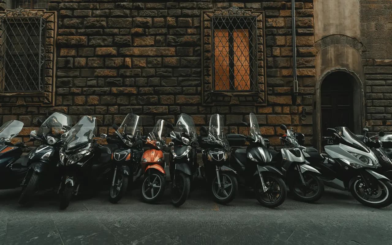 Rangée de motos et de scooters garés en épi le long d’un mur de pierre, sur le trottoir d’une rue de ville déserte.