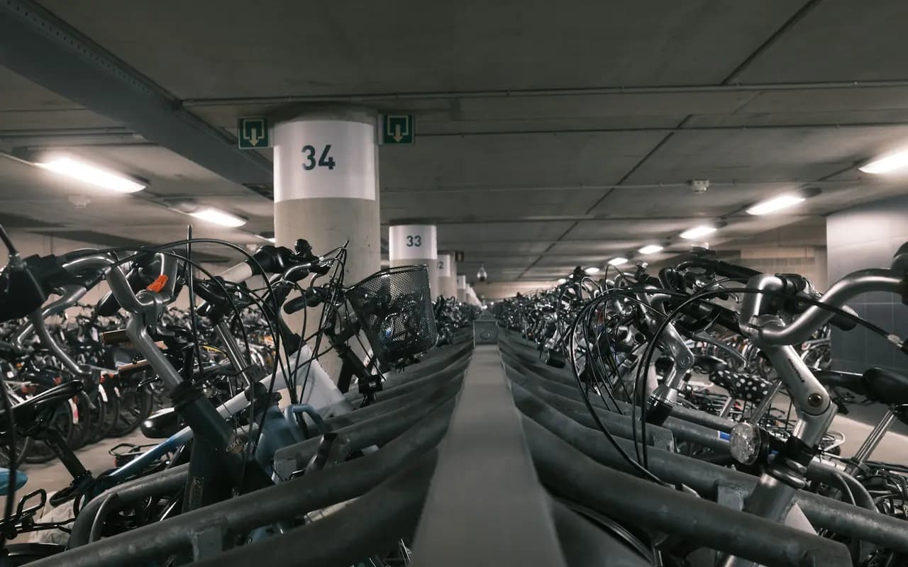 Deux allées de râteliers à double étage remplis de vélos de ville dans un parking souterrain éclairé au néon.