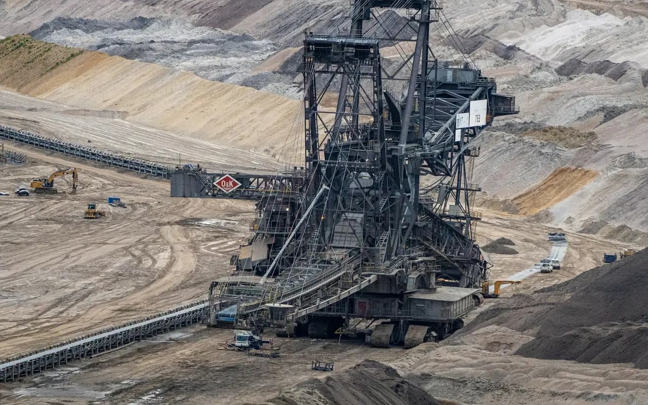 Excavatrice à roue-pelle au fond d’une mine à ciel ouvert, gradins de terre nue à perte de vue et convoyeur remontant vers le haut de la fosse.